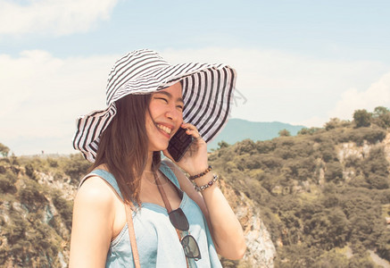 身戴帽子用手机聊天的亚洲美丽女前往山地背景模糊的暑假旅行时使用手机交谈游客称呼徒步旅行图片