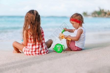 两个小女孩在白色热带海滩上做沙堡背景