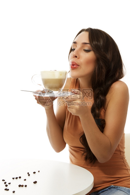 女青年吹到热卡布奇诺咖啡坐在桌子上白色背景的桌子上成人女士早餐图片