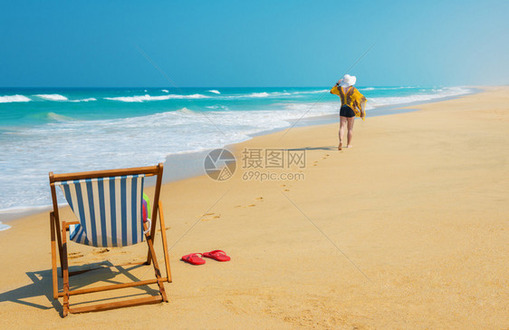 太阳帽甲板椅和穿白衣女人沿着海滩游荡图片