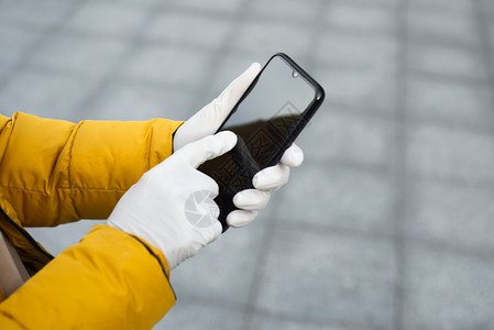 人们年轻的Corona传播预防措施概念在公共场所的街上持有移动电话的年轻妇女手持移动电话身着乳胶保护手套在街头佩戴乳胶保护手套在图片