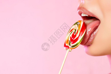 一位年轻美丽的女孩舔着一个多彩明亮的洛利波普Lollipopop她用的舌头在粉红色孤立的背景和复制空间上近距离拍摄嘴魅力吸图片