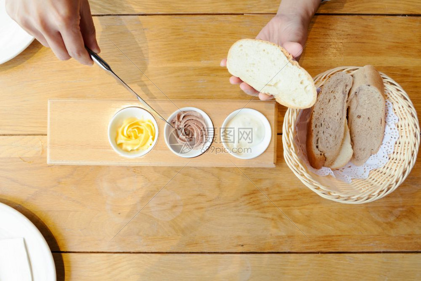 女士法国面包粉妇女用手在切片面包上撒黄油图片