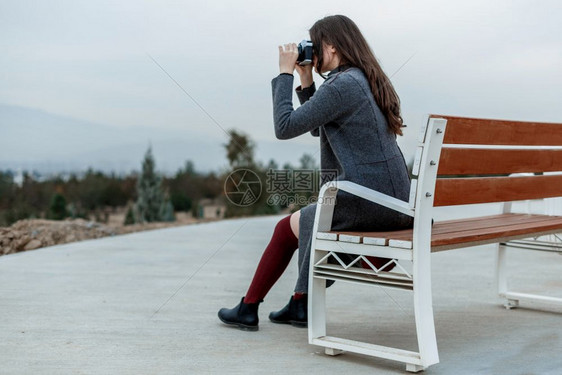 肖像户外在勃伦迪丝袜和灰色大衣的年轻美少女坐在白长椅上日落时有摄像头成人图片