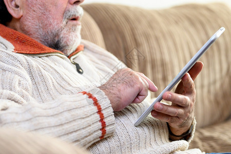 坐着老人在沙发上并客厅使用数字平板电脑的特写肖像老人坐在沙发上并客厅使用数字平板电脑的特写肖像阅读快乐的图片