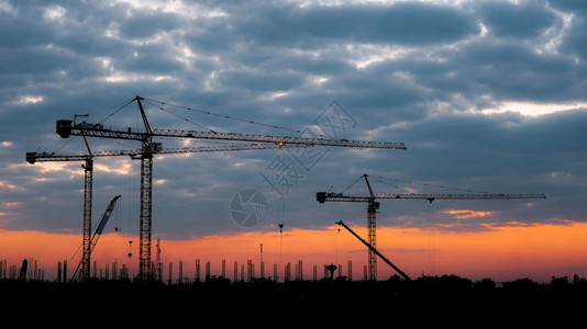 日落时塔式起重机和大型建筑工地的剪影日落背景下有起重机的新建筑工地暮机器团队合作图片