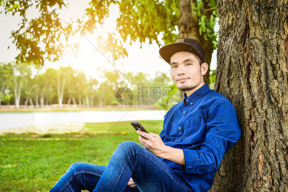 手指公司的绿色蓝衬衫人使用智能手机上网各地的科技社交媒体及自然背景阳光在网络上使用智能手机图片