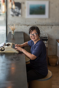 亚洲女四十多岁白皮肤眼镜和坐在一个亚洲女咖啡馆厅用旧式打字机写作的东西上一位亚洲女则在一家咖啡店用打字机眼镜写作工泰国快乐的图片
