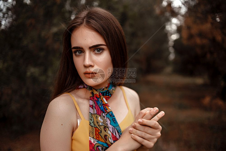 一个年轻美丽的女孩肖像身着黄色洋装带彩多的围巾站在树林里金子仙女春天图片