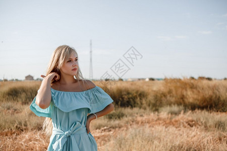 身着浅蓝色礼服的美丽古巴年轻金发女孩站在田地上带着阳光遮的草地女微笑人们图片