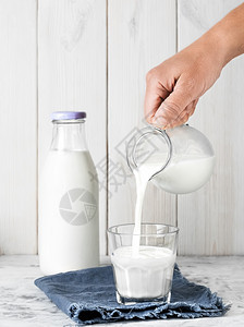 食物牛奶从罐头倒入玻璃中奶瓶放在白木背景的色牛奶上密闭早餐概念健康食品可再用玻璃器械从罐子倒入玻璃白色的商品图片
