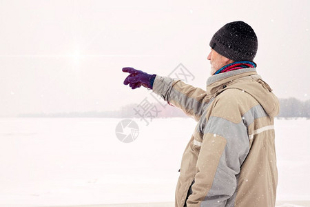 一个戴羊毛帽防水夹克和羊毛帽的男人在雪下寒冷而悲伤的冬季清晨用手指靠近第尼珀尔河指着一些东西灰色的防水寒冷图片