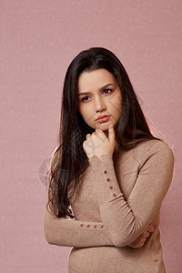 人们怀疑常设一个年轻美丽的亚洲黑发女肖像穿着浅棕色毛衣想着一个粉红孤立的背景带复制空间的事物图片