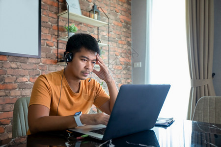 屋操作员一种亚洲男人使用笔记本电脑在家里努力工作开会而且压力很大头痛图片