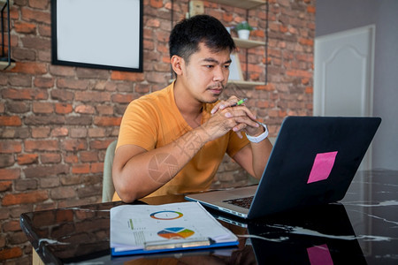 亚洲男人使用笔记本电脑在家里努力工作开会而且压力很大头痛新的学习顾问图片
