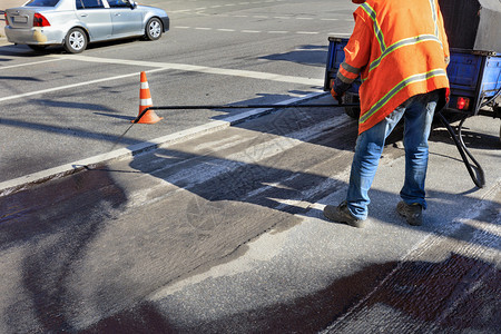 巷道服务路维修工人将沥青混合物喷洒到清洁地区以更好粘附新的沥青工人喷洒表面上的对路进行部分修复筑沥青路装勤杂工图片