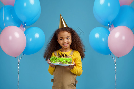 甜的女oopicapi戴帽子的有趣小女孩拿着生日蛋糕蓝背景的色漂亮的女孩得到了一个惊喜活动庆祝气球装饰戴着帽子的有趣小女孩拿着生图片