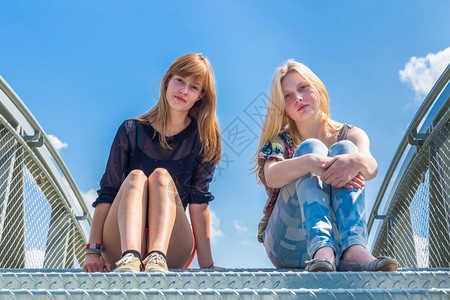 荷兰语微笑青少年坐在蓝色天空的金属桥上两个荷兰女青年友们图片