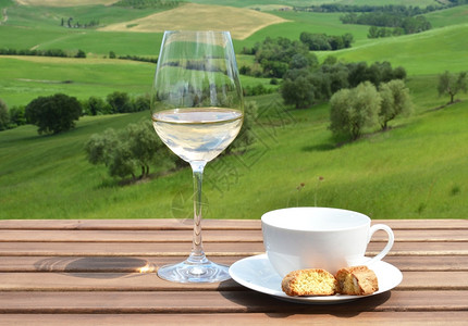 木制的方格写与意大利托斯卡纳橄榄园对抗的木制桌上咖啡杯罐头和白葡萄酒图片