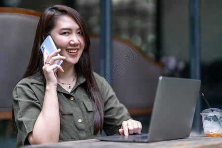 女商人在咖啡店用笔记本电脑工作时用咖啡杯和智能手机如背景通信概念等在咖啡店里捡起智能便携机的空闲手写作女士嗓音吸引人的图片