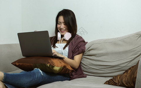 活的肖像人使用笔记本电脑和耳机的亚洲年轻美女在家用生活风格技术和新常识概念客厅休息时使用笔记本电脑和耳机图片