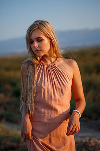 时髦一位年轻美丽的白人金发女肖像穿着粉红裙子在荒野中面对日落冷清趋势图片