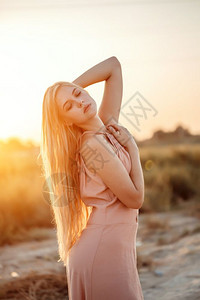 时髦的一位年轻美丽白人金发女肖像穿着粉红裙子在荒野中面对日落常设户外图片