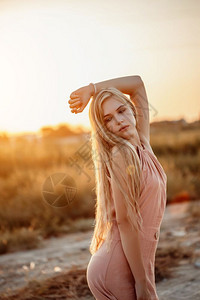 趋势淑女一位年轻美丽的白人金发女肖像穿着粉红裙子在荒野中面对日落一种图片