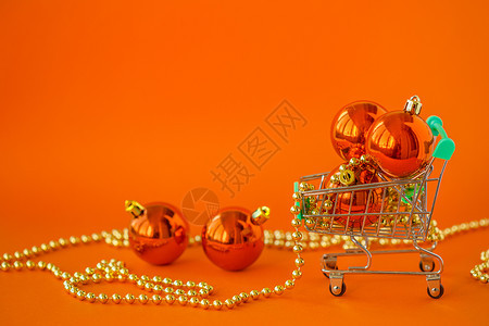 手推车象征一种圣诞礼物球在橙色轮椅和装饰上以橙色背景的圣诞和新年销售圣诞礼品在线商店小型轮车和橘色背景的圣诞和新年销售中以果实形图片