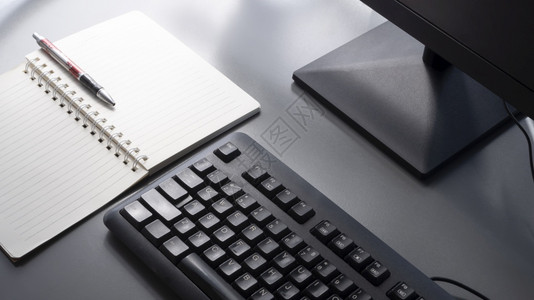 互联网移动的有选择地聚焦于黑键盘上带有部分计算机监视器圆点笔和螺旋记板的黑键盘上灰面桌有阳光和表阴影商业图片