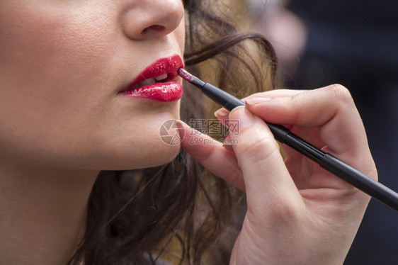 光滑一种化妆师在年轻女人的嘴上涂唇膏闪亮的图片