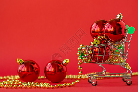 庆典在微型手推车中赠送圣诞球和红色背景上的装饰品欣喜若狂玩具图片
