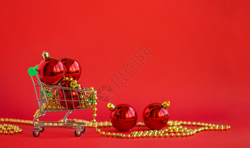 在微型手推车中赠送圣诞球和红色背景上的装饰品快乐圣诞老人图片