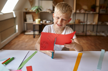 令人愉快的工作铅笔小男孩在桌子上剪彩纸在车间里的孩子艺术学校的创意课年轻画家愉快爱好乐童年小男孩在车间里剪彩纸图片