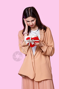 失望的女朋友周年纪念日一个轻女孩穿着一件外套手里拿着一个礼品盒的物对粉红色孤立的背景感到不满和失望图片