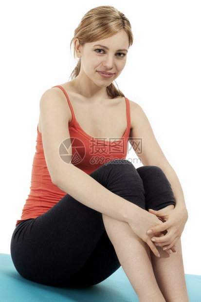 娱乐女士微笑年轻健身女子坐在蓝色长着的垫子上在白色背景的蓝垫子上停一下图片