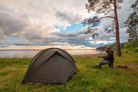 水在湖岸露营帐篷附近玩吉他享受观光的旅游者与自然团结美丽的宁静图片