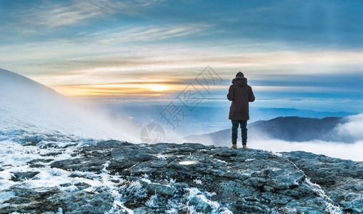 一个人站在白雪覆盖的悬崖上俯瞰日落下的山脉壮丽景色旅行美的假期图片