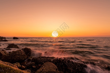 日落时天际线上的大太阳海水溅在岩石滩上美丽的夕阳天空和橙色的云彩海浪在夏日岸的石头上溅起自然景观热带海夏天假期洋图片