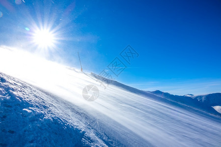 自然霜强烈的风吹起许多雪尘在太阳中闪耀着光下的雪暴在天晴时空滑雪斜坡上地形图片