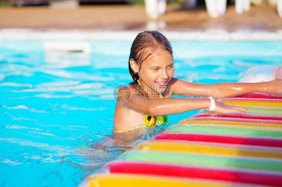 采取笑微小女孩在游泳池玩耍和乐与空气床垫一起游泳小孩在水里玩游泳概念女孩在暑假度时池游泳图片