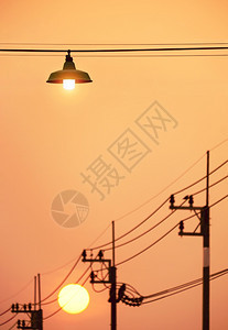 日出路灯金属丝对面的电线杆模糊在垂直框架的日落天空背景下使用紫色挂着吊上街灯的悬浮光柱图片
