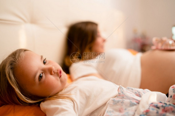 孩子电话服用女和怀孕母亲躺在家中的床上等待男婴或女在医院出生分娩图片