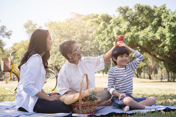 女亚洲家庭与儿子一起坐在公共园头顶的苹果上方亚裔家庭在节日快乐时生活方式概念美丽的陈年图片