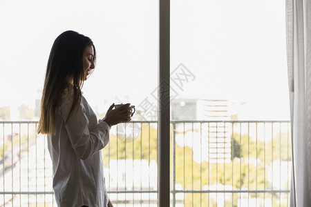 站在阳台上的快乐女人握着咖啡杯手黑发情绪化的阳光图片