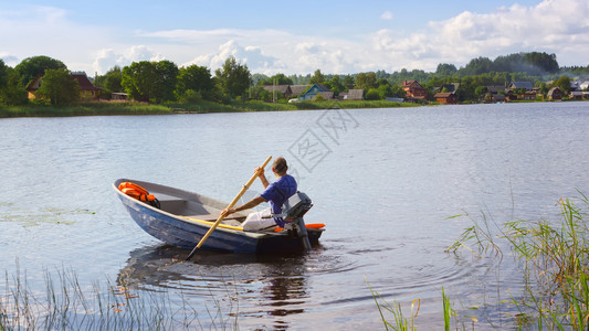 一名男子身在艘挂着桨的机动船上漂浮在湖边与远海岸相对有村庄房屋俄罗斯塞里格湖旅游度假休闲爱好和户外活动空间的概念可复制选择地聚焦背景图片