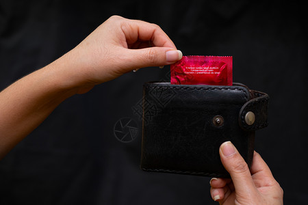 精子近身妇女手握黑色皮衣钱包底带红色避孕套安全行为和保健以及医疗概念情人节安全与保健艾滋爱图片