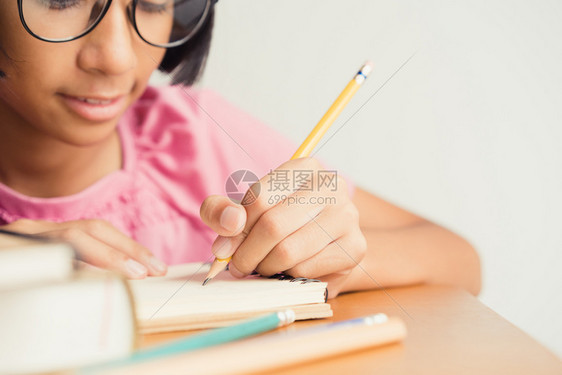 课亚裔小女孩在家坐书桌上写字时戴着眼镜纸童年图片