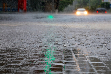 湿的车头灯光照亮了人行道和沥青路上的大雨路口的绿色交通灯照亮了汽车光路口的绿色交通灯光照亮了城市街道上的大滴子和一条水流图片