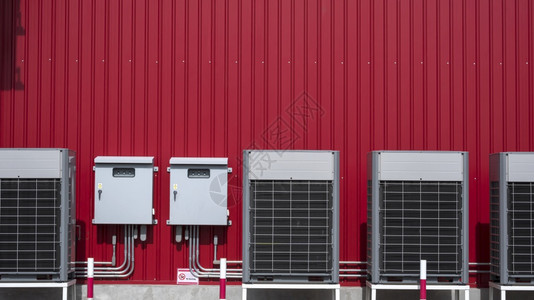 行业灰色的库建筑物外红金属板墙上装有2个电控柜和输管道系统的空调压缩机一行系统和2个电控制柜输管道系统图片